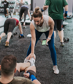 Female trainer holding phone and coaching man doing sit ups