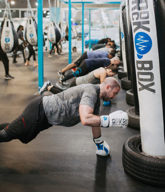 Row of people doing push ups with boxing gloves on in front of boxing bags