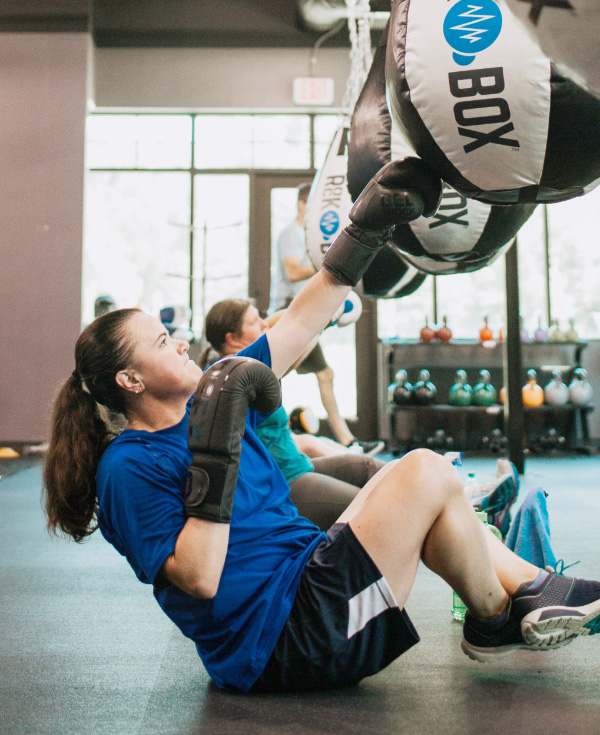 woman sitting on the ground, engaging her core, hitting a punching bag above her